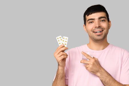 Young man with water pointing at blisters of vitamin A pills on light backgroundの写真素材