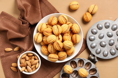 Bowl with tasty walnut shaped cookies, almonds and baking form on beige wooden table