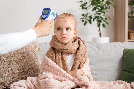 Sick little girl and her mother with infrared thermometer measuring temperature at home
