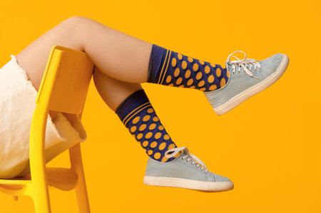 Young woman in stylish sneakers sitting on chair against yellow background