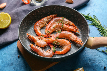 Frying pan with tasty shrimps and lemon on blue backgroundの写真素材