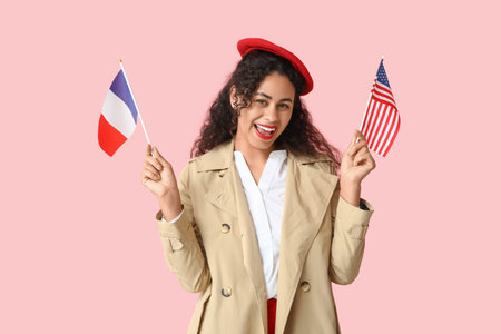 Beautiful young happy African-American woman with USA and France flags on pink background