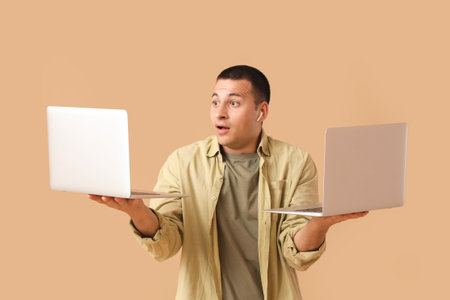 Handsome young shocked man with laptops on beige backgroundの写真素材