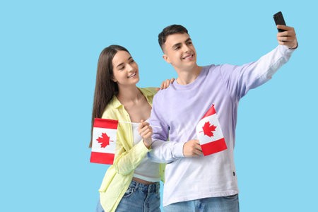 Young couple with flags of Canada taking selfie on blue backgroundの写真素材