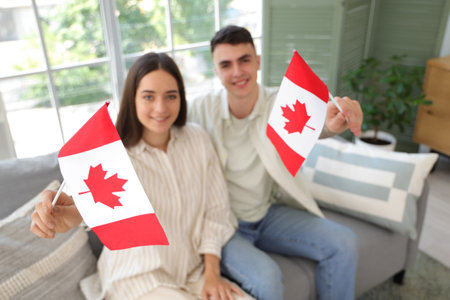 Young couple with flags of Canada sitting on sofa at homeの写真素材