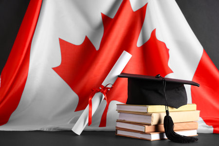Stack of books, graduation hat, diploma and Canadian flag on dark backgroundの写真素材