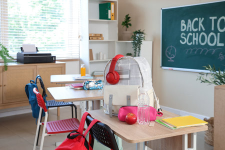 Backpack with headphones, apple and water bottle on desk in classroomの写真素材