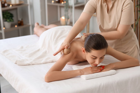 Young woman getting back massage with wooden balls on couch in spa salonの写真素材