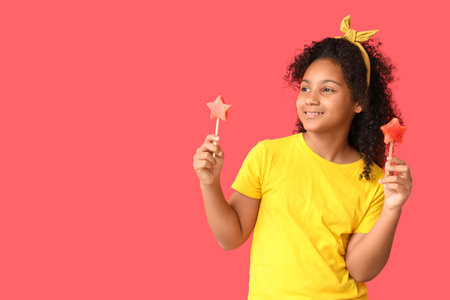 Cute African-American girl holding sticks with sweet watermelon in shape of stars on red backgroundの写真素材