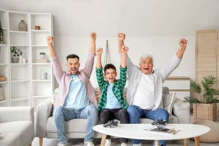 Happy teenage boy with his dad and grandfather playing video game on sofa at homeの写真素材