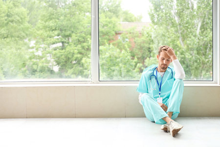 Tired medical intern sitting near window in clinicの写真素材