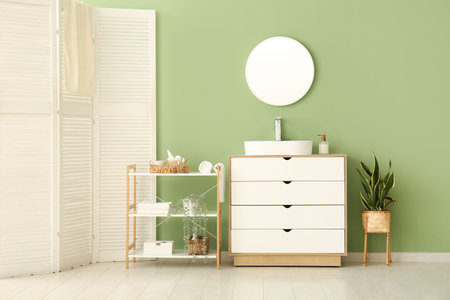 Ceramic sink, shelving unit and white chest of drawers near green wall in stylish bathroom