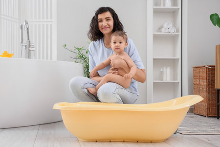 Mother with her little baby near bathtub at home