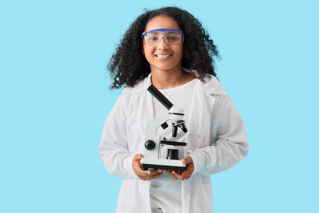 Little African-American schoolgirl with microscope on blue backgroundの写真素材