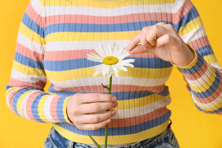 Young woman with chamomile flower on yellow background, closeupの写真素材