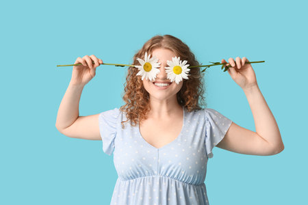 Beautiful young woman with chamomile flowers on blue backgroundの写真素材