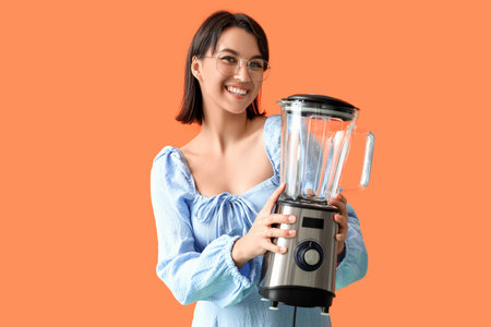 Young woman with blender on orange backgroundの写真素材
