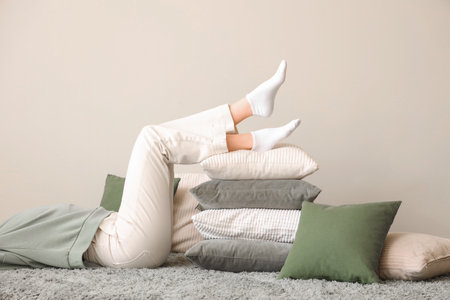 Young woman lying on floor with stack of soft pillows in stylish roomの写真素材