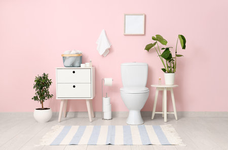 Toilet bowl, bedside table and plants near pink wall in restroomの写真素材