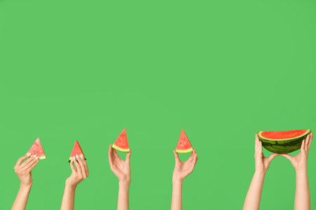 Female hands with many pieces of sweet watermelon on green backgroundの写真素材