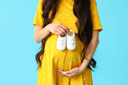 Young pregnant woman with baby boots on blue background