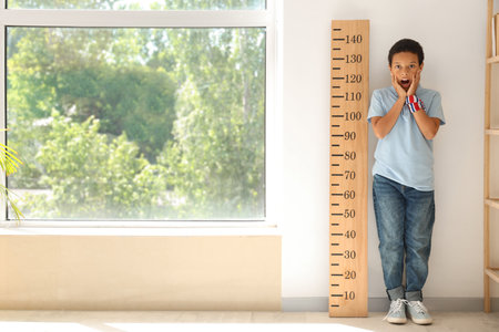 Shocked little African-American boy measuring height near stadiometer at homeの写真素材