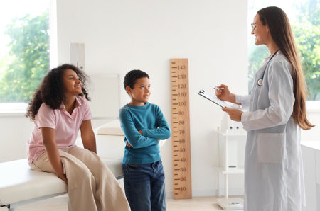 Female pediatrician with little African-American children measuring height in clinicの写真素材