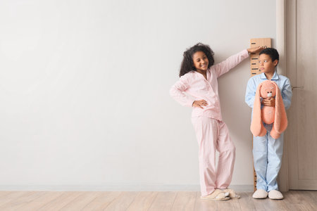 Little African-American girl measuring her brother's height near stadiometer at homeの写真素材