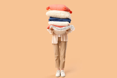 Beautiful young woman with stack of different blankets and pillows on beige backgroundの写真素材