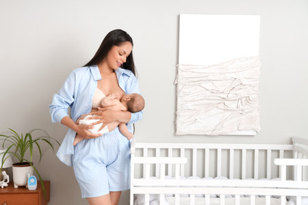 Beautiful young happy woman breastfeeding her baby in bedroom at homeの写真素材