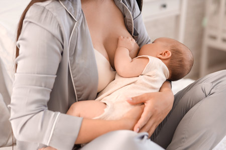 Beautiful young woman breastfeeding her baby at home, closeupの写真素材