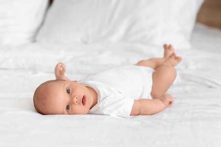 Cute little baby lying on bed in room at homeの写真素材