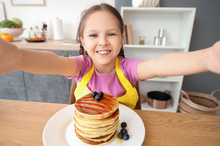 Cute little girl with pancakes and honey taking selfie in kitchenの写真素材