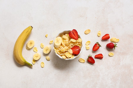 Banana, bowl with cornflakes and strawberries on light backgroundの写真素材