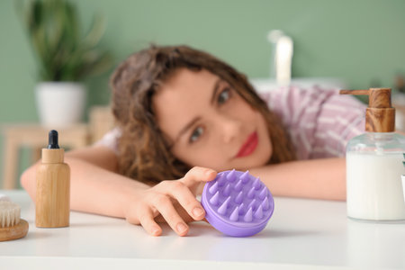 Young woman with hair scalp massager at table in bathroom, closeupの写真素材