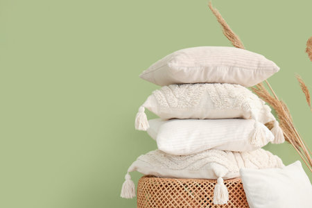 Wicket basket with stack of pillows and pampas grass near green wall