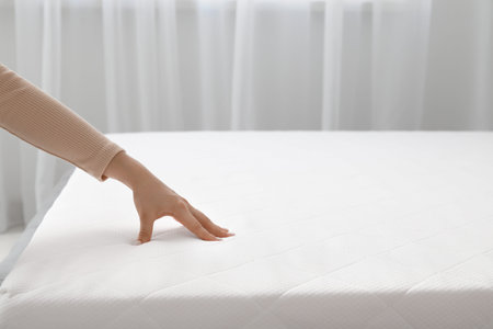 Woman touching soft orthopedic mattress on bed at home, closeup