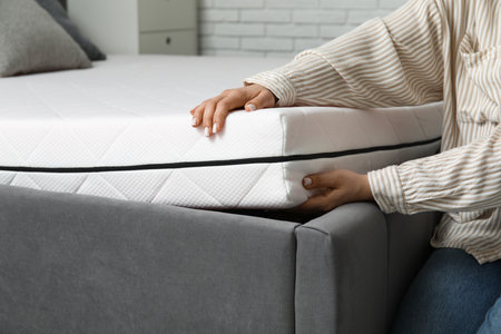 Woman putting soft orthopedic mattress on bed at home, closeupの写真素材
