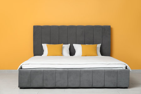 New orthopedic mattress with blanket on stylish bed near yellow wall in roomの写真素材
