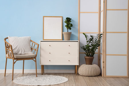 Interior of room with folding screen, commode and wicker chair near blue wall