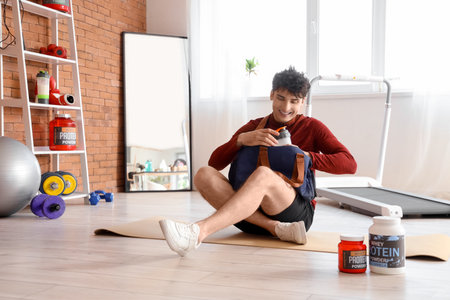 Sporty young man taking protein shake from bag in gymの写真素材