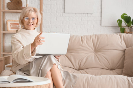 Middle-aged woman with laptop sitting on sofa at homeの写真素材