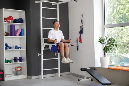 Sporty young man training on wall bars in gym