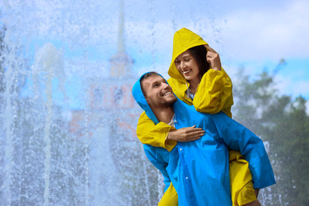 Happy young couple wearing raincoats on rainy day outdoorsの写真素材