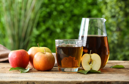 Glass and jug of fresh apple juice on wooden table outdoorsの写真素材