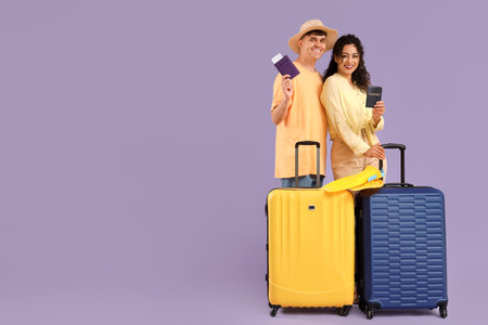 Happy young couple with suitcases and passports on lilac backgroundの写真素材