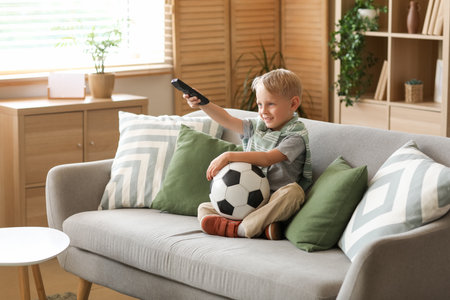 Cute little football player with soccer ball watching TV at homeの写真素材