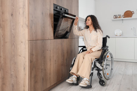 Young African-American woman in wheelchair opening oven at homeの写真素材