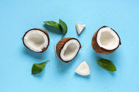 Halves of fresh coconuts and leaves on blue background