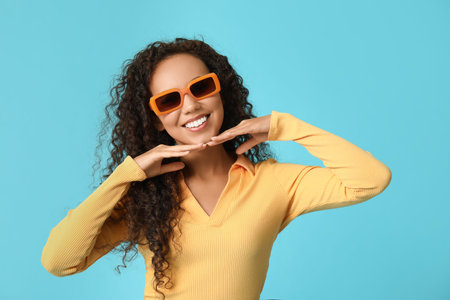 Happy young African-American woman in sunglasses on blue backgroundの写真素材